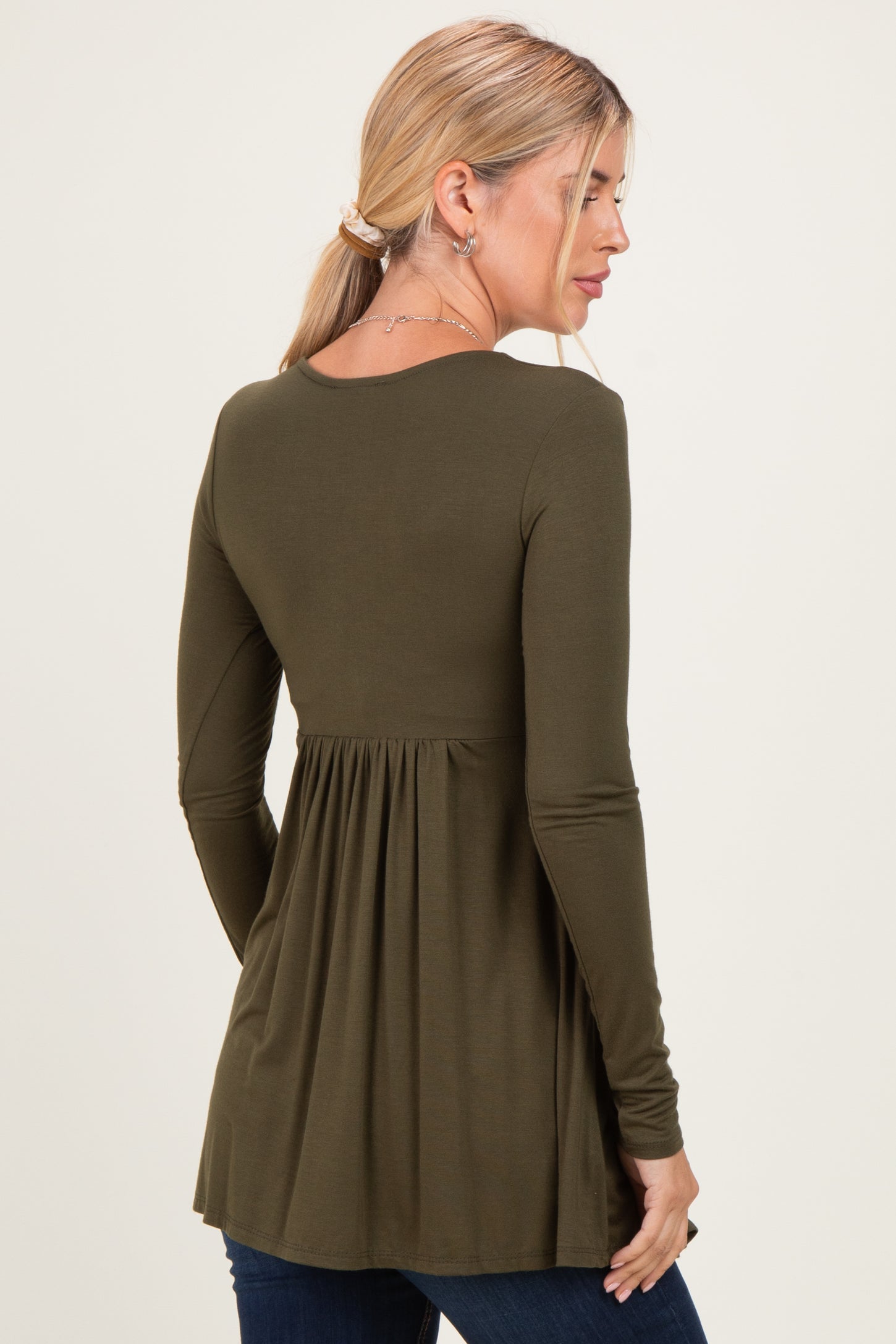 woman wearing an olive green long sleeve top with a pleated back and a relaxed fit