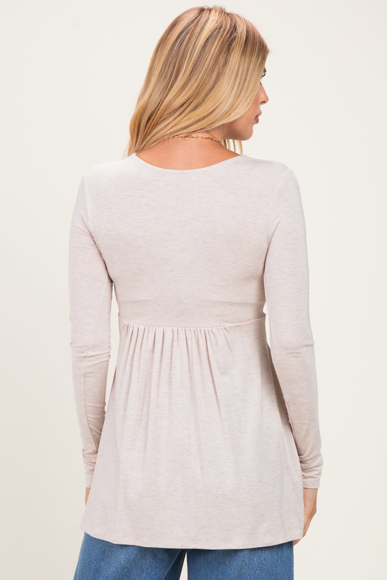 woman wearing a light taupe long sleeve peplum top with a round neckline and back pleat detail