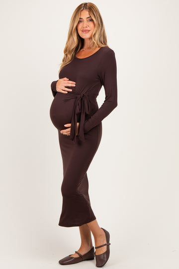 woman wearing a dark brown long sleeve maternity dress with a tie detail, showcasing her baby bump