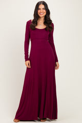 woman wearing a burgundy long sleeve maxi dress with a fitted bodice and a flowing skirt