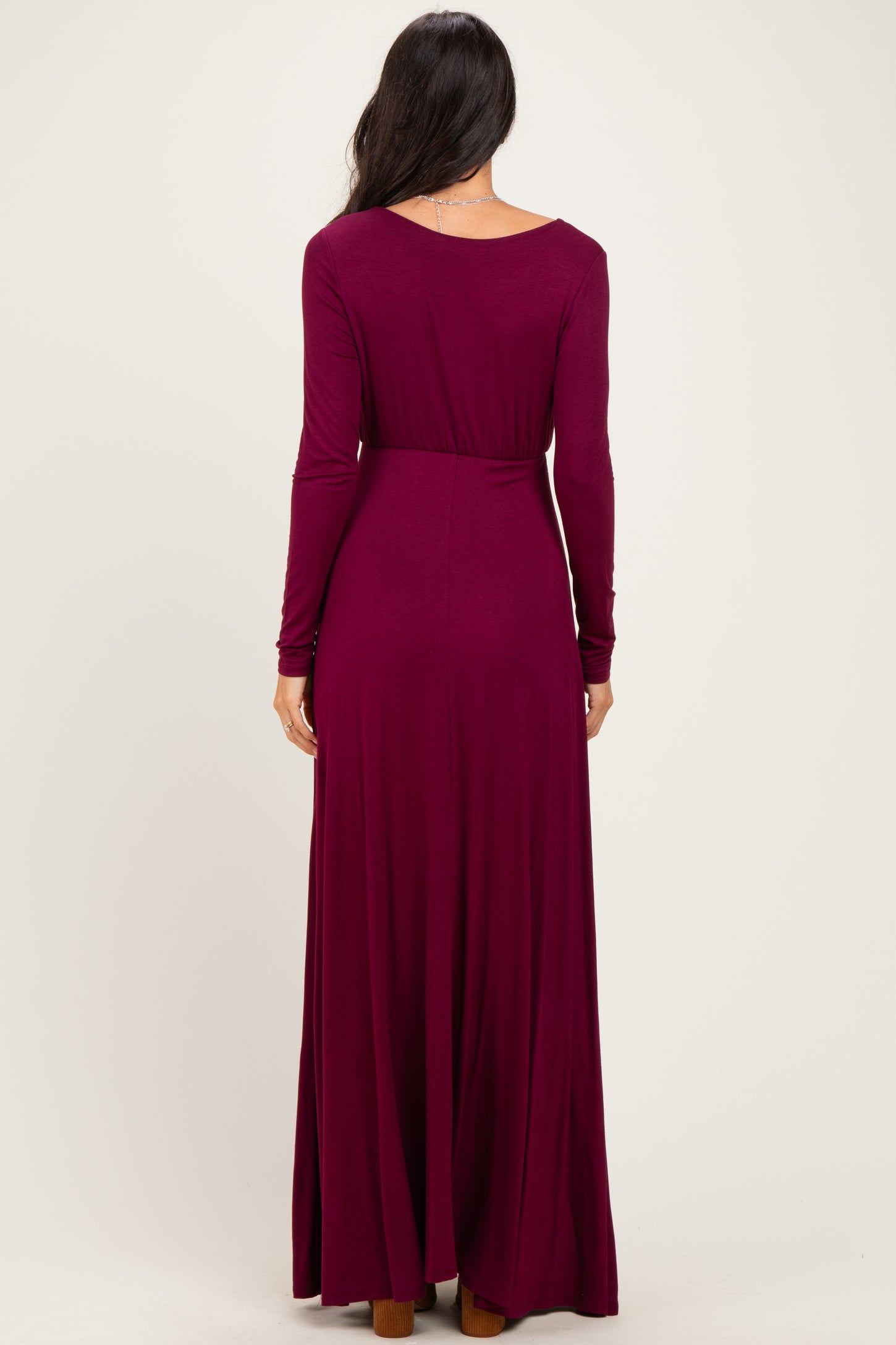 woman wearing a long burgundy maxi dress with long sleeves and a fitted waist, shown from the back