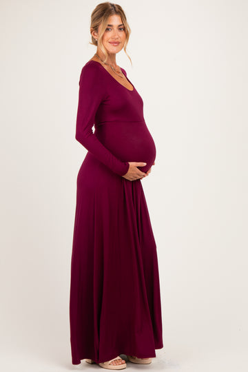 woman wearing a burgundy long sleeve maternity maxi dress and holding her baby bump