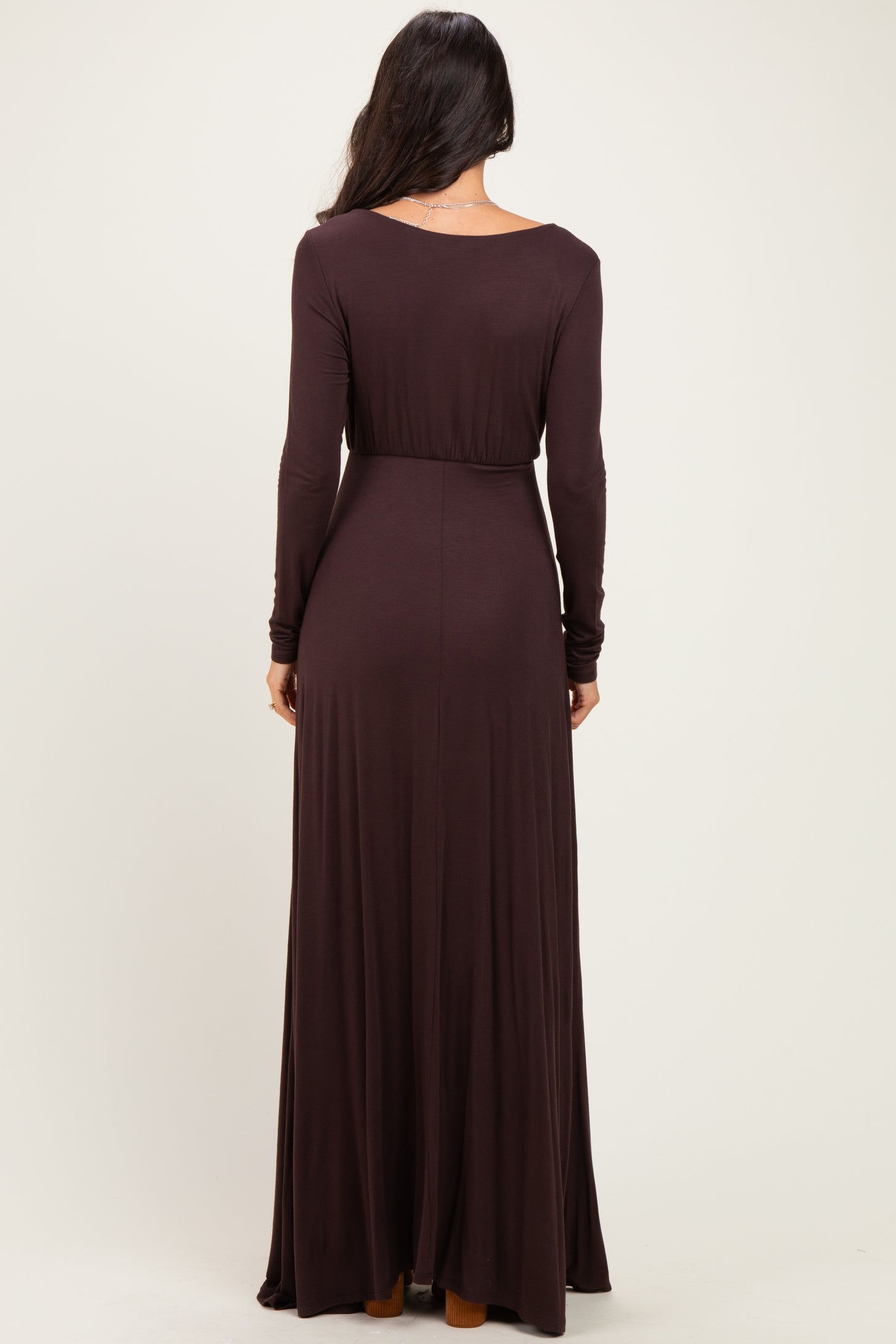 woman wearing a long sleeve dark brown maxi dress with a fitted waist and flowing skirt, seen from the back