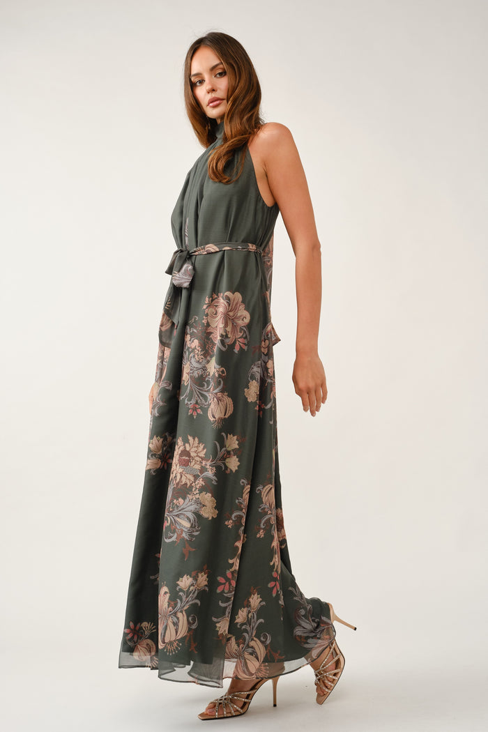 woman wearing a dark green maxi dress with floral print and belted waist, posing with one leg slightly forward