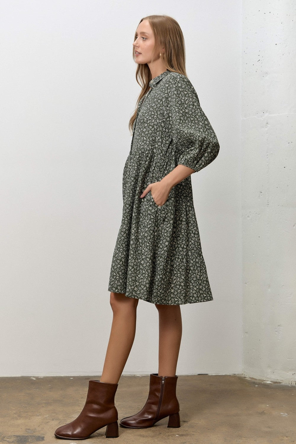 woman wearing a dark green floral print dress with three-quarter sleeves and pockets, paired with brown ankle boots