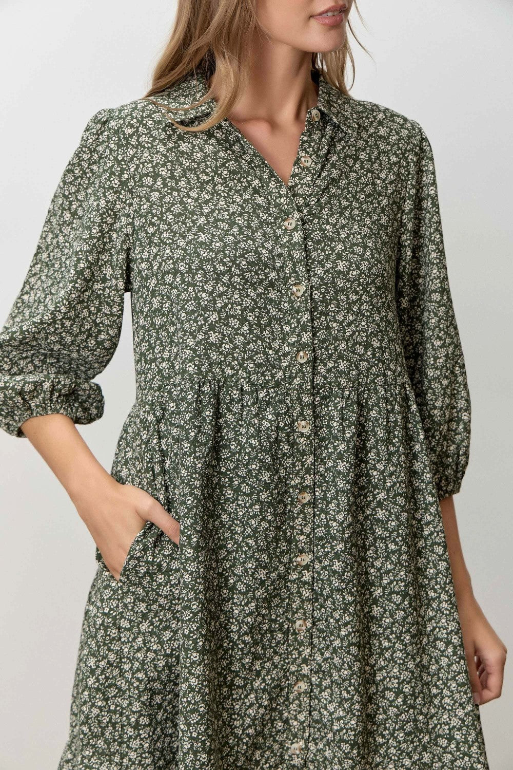 woman wearing a green floral print button-up dress with three-quarter sleeves and pockets