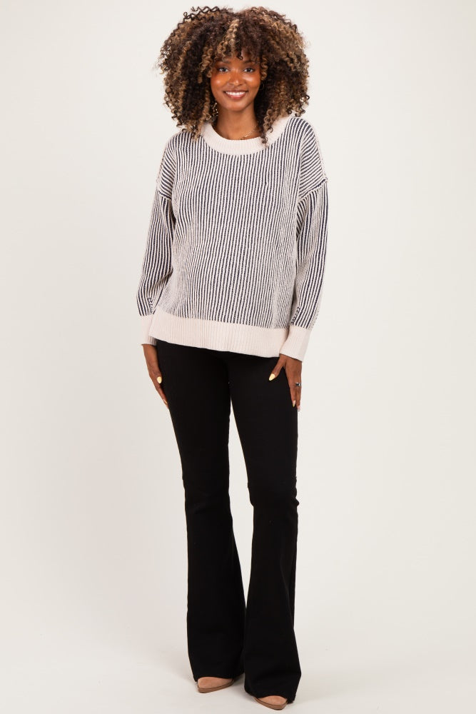 woman wearing a striped black and white maternity sweater with wide sleeves and black flared pants