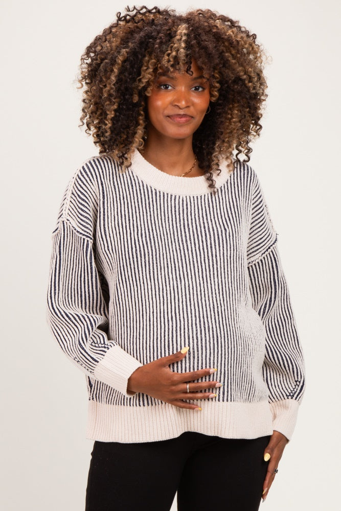 woman wearing a striped maternity sweater in cream and black, holding her baby bump