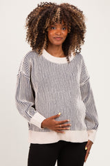 woman wearing a striped maternity sweater in cream and black, holding her baby bump