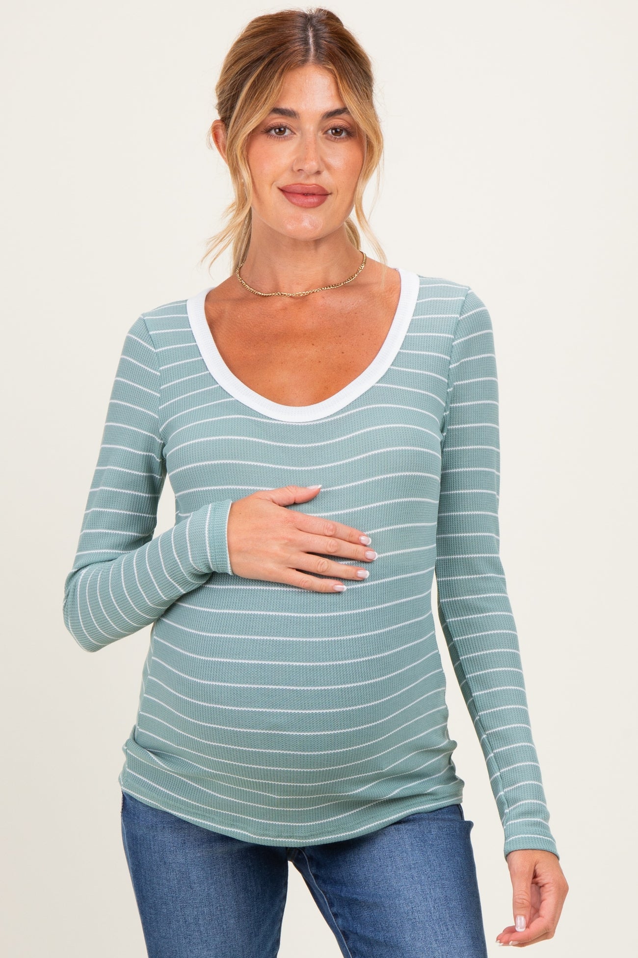 woman wearing a green striped maternity top with a white neckline and holding her baby bump