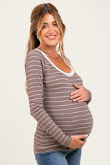 woman wearing a brown striped maternity top and cradling her baby bump