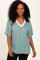 woman wearing a green striped short sleeve top with a v-neck and pocket, smiling at the camera