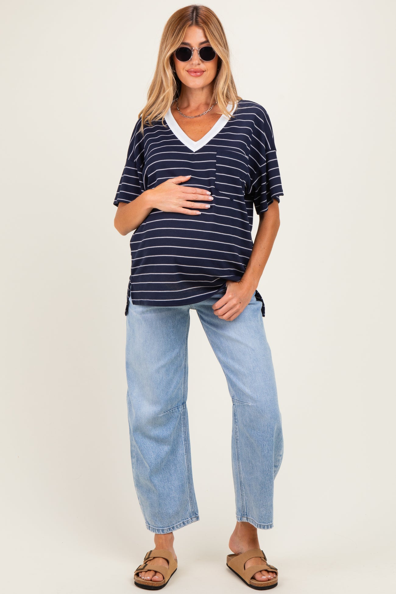 woman wearing a navy and white striped maternity top with a v-neck and holding her baby bump, paired with light blue wide-leg jeans