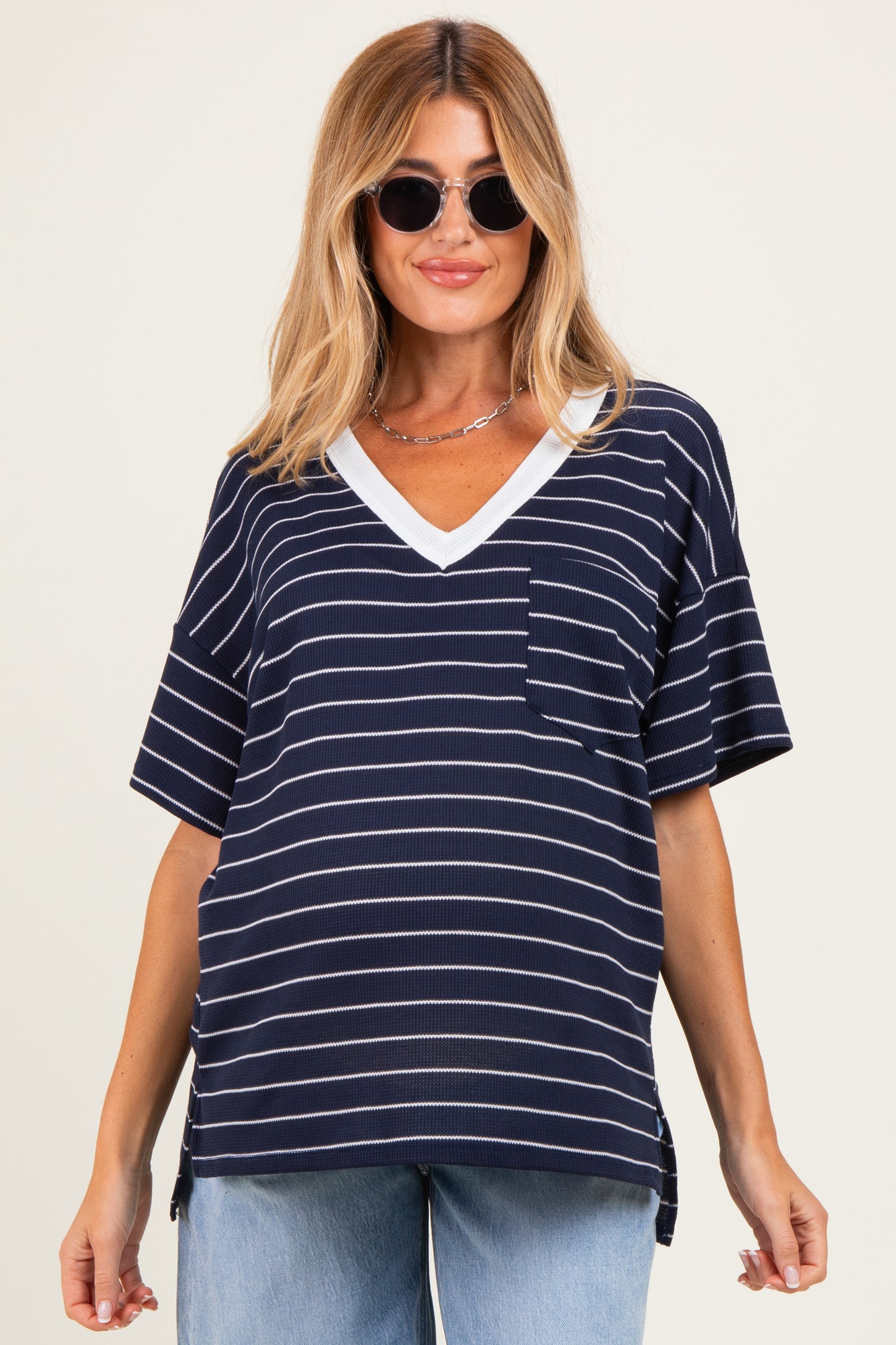 woman wearing a navy and white striped maternity top with a v-neck and pocket, styled with sunglasses and relaxed jeans