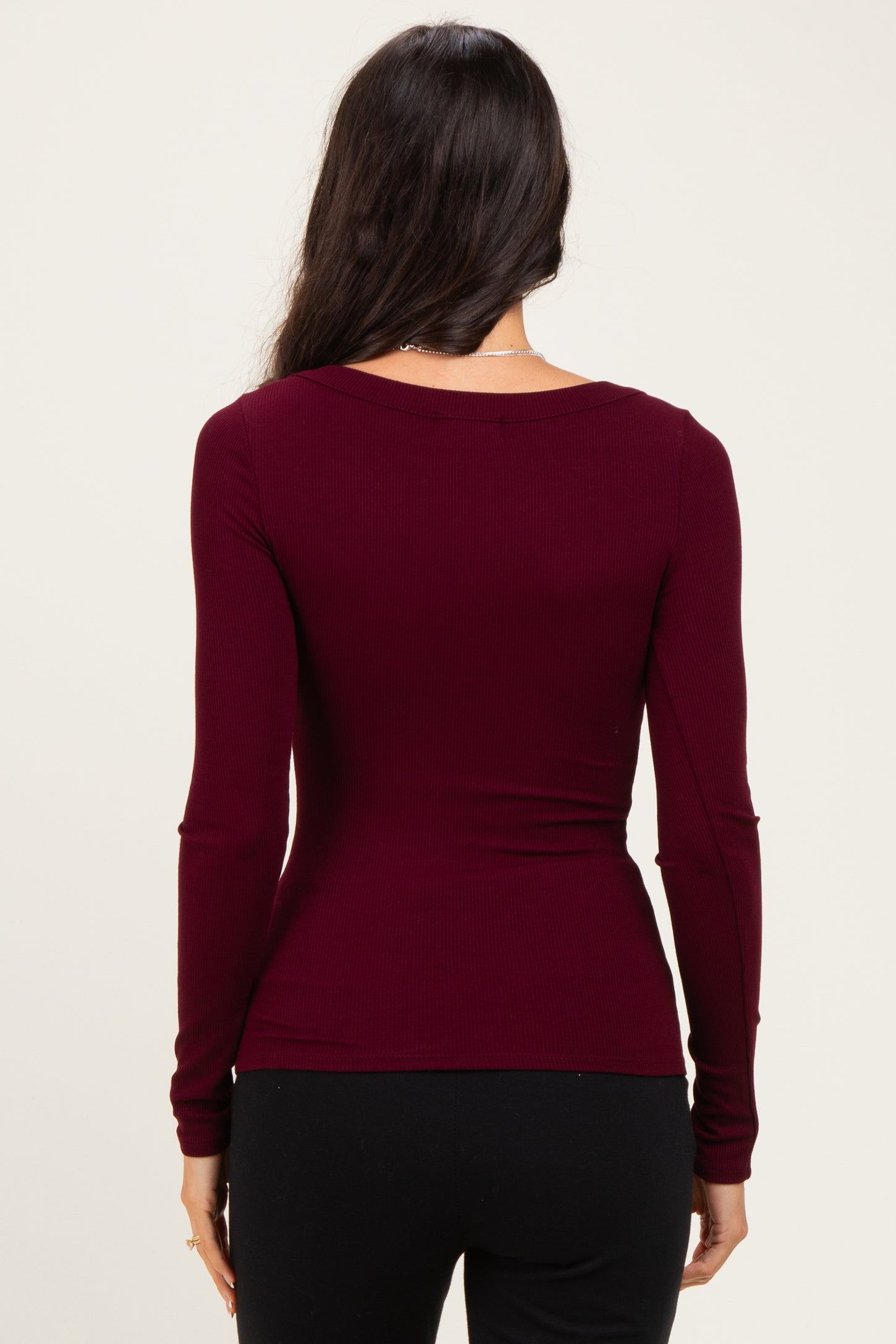 woman wearing a burgundy long sleeve fitted top, viewed from the back