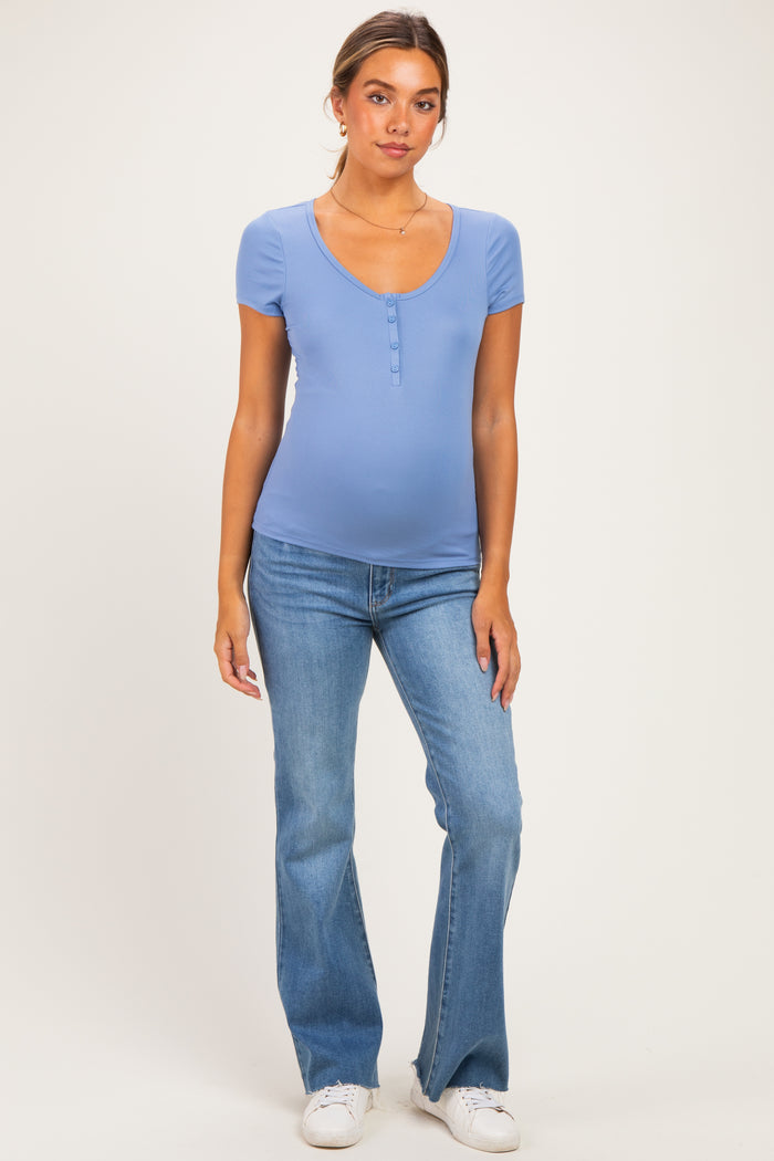woman wearing a light blue maternity top with short sleeves and a scoop neckline, paired with flare jeans and showing her baby bump