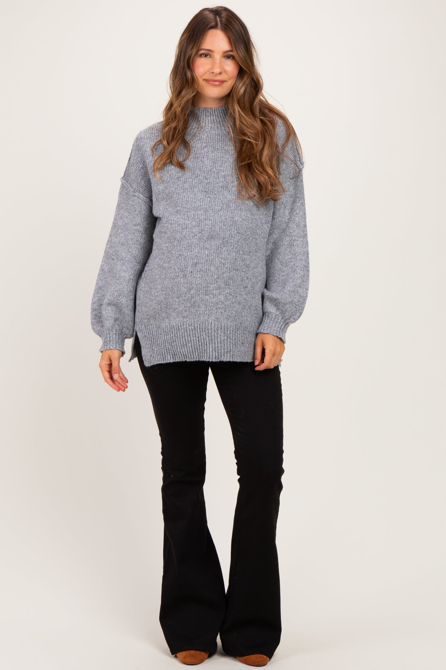 woman wearing a light grey oversized maternity knit sweater and black flared pants, no visible baby bump