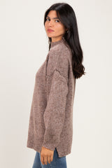 woman wearing a taupe oversized sweater with a mock neck and ribbed hem, styled with blue jeans