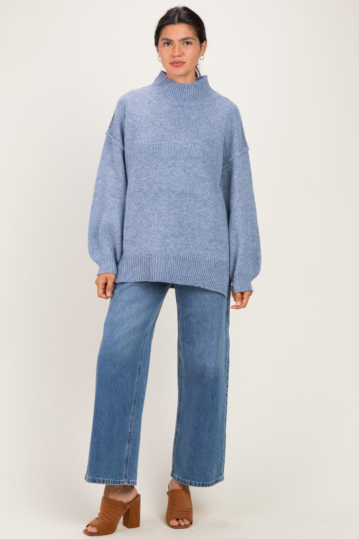 woman wearing a light blue oversized sweater with a mock neck and wide-leg jeans, standing in brown block-heeled sandals