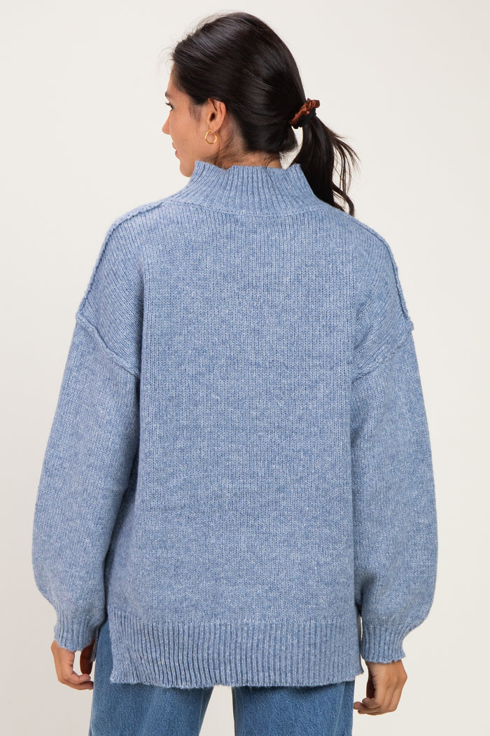 woman wearing a light blue oversized sweater with a high neck and drop shoulder sleeves