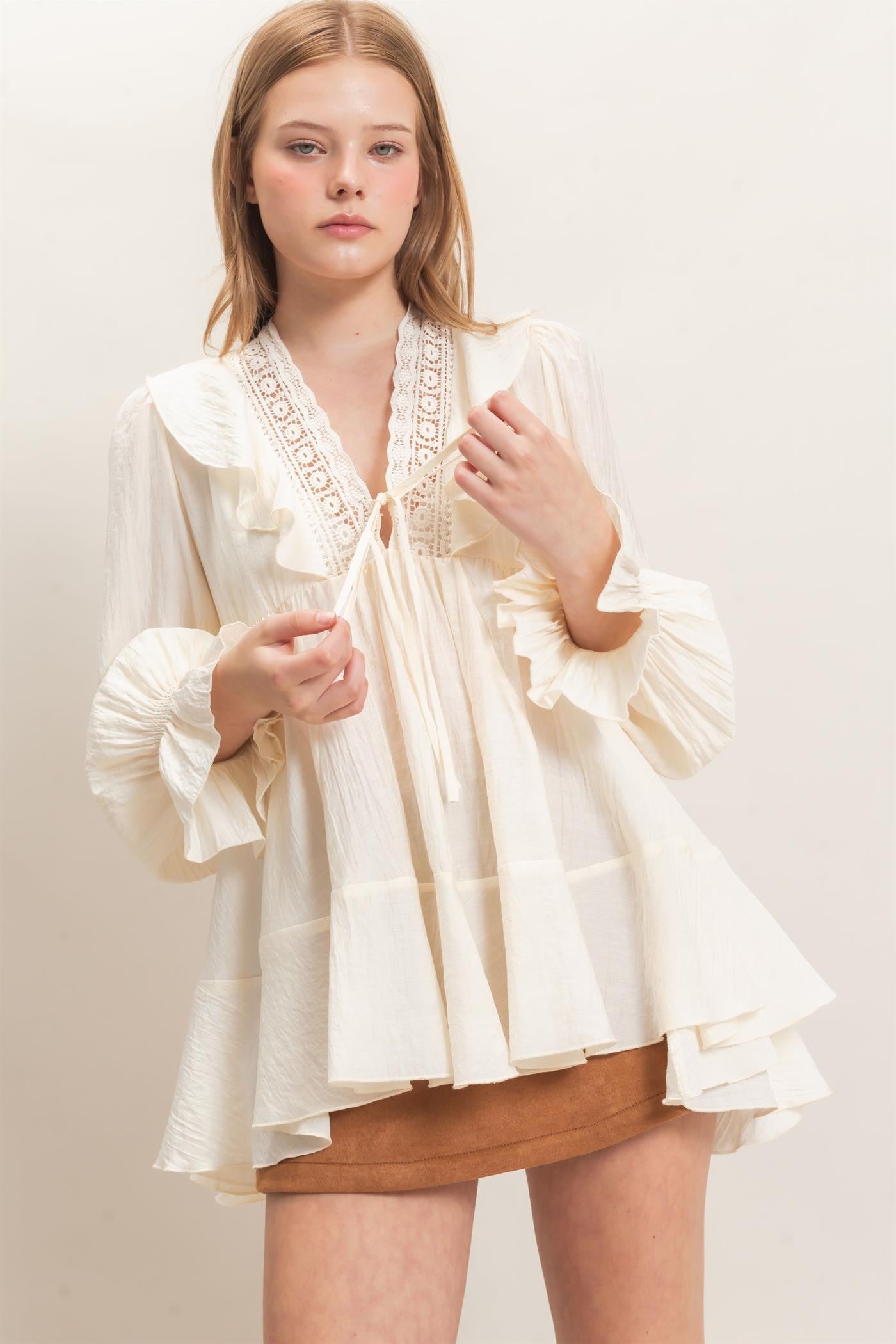 woman wearing a cream ruffled blouse with lace detailing and balloon sleeves, paired with a brown mini skirt