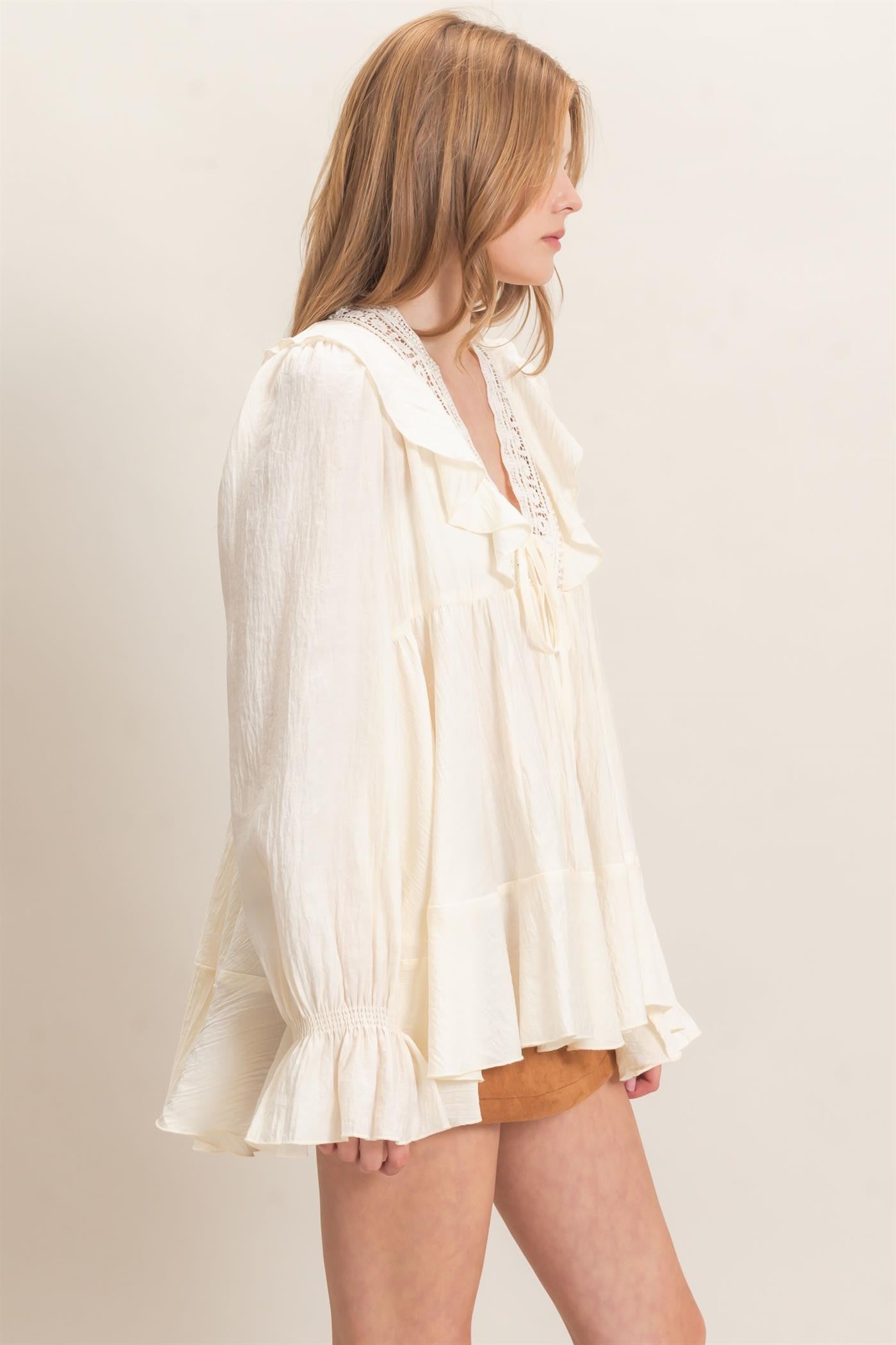 woman wearing a cream tiered blouse with ruffle details and a lace trim, paired with a brown suede mini skirt