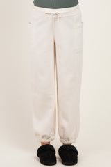 woman wearing cream-colored maternity sweatpants with pockets and elastic cuffs, standing in plush slippers