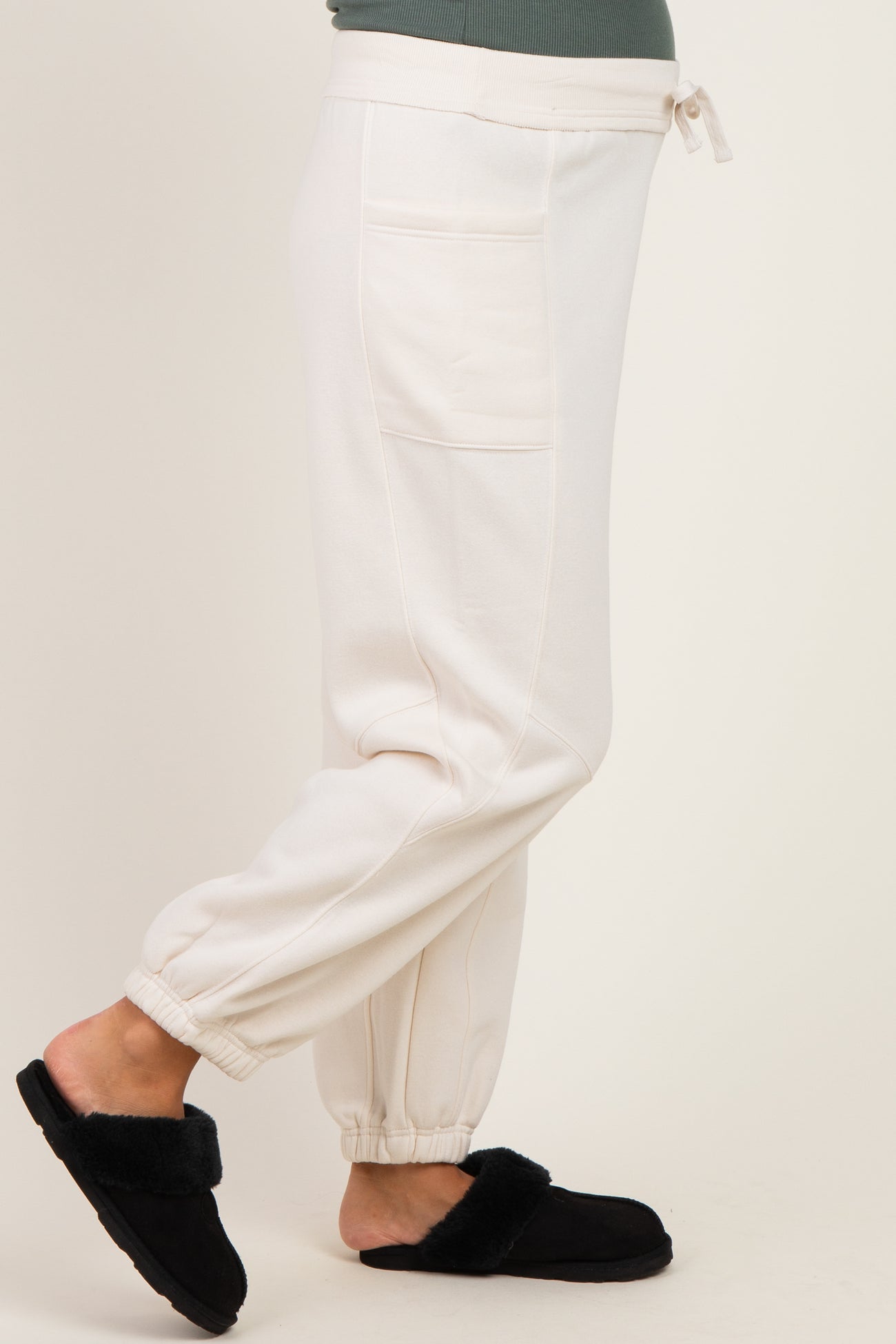 woman wearing white maternity jogger pants with pockets and adjustable waist, paired with black fuzzy slippers