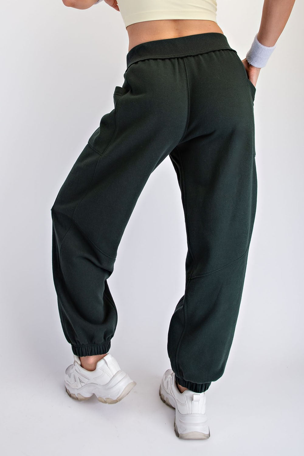 woman wearing dark green sweatpants with elastic cuffs and pockets, styled with a beige crop top and white sneakers