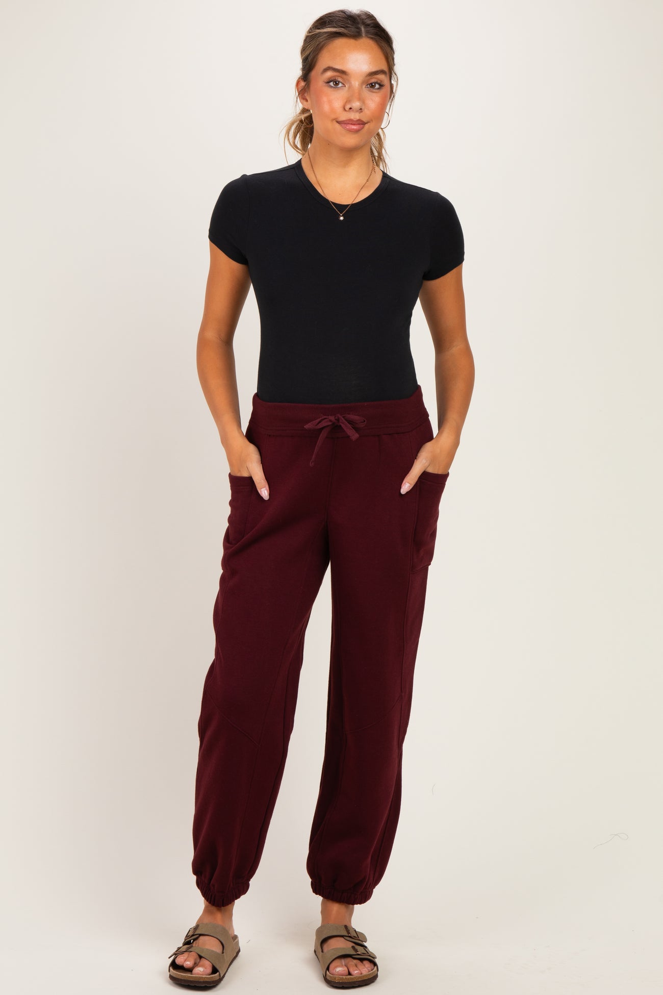 woman wearing a black short sleeve maternity top and burgundy maternity jogger pants with side pockets