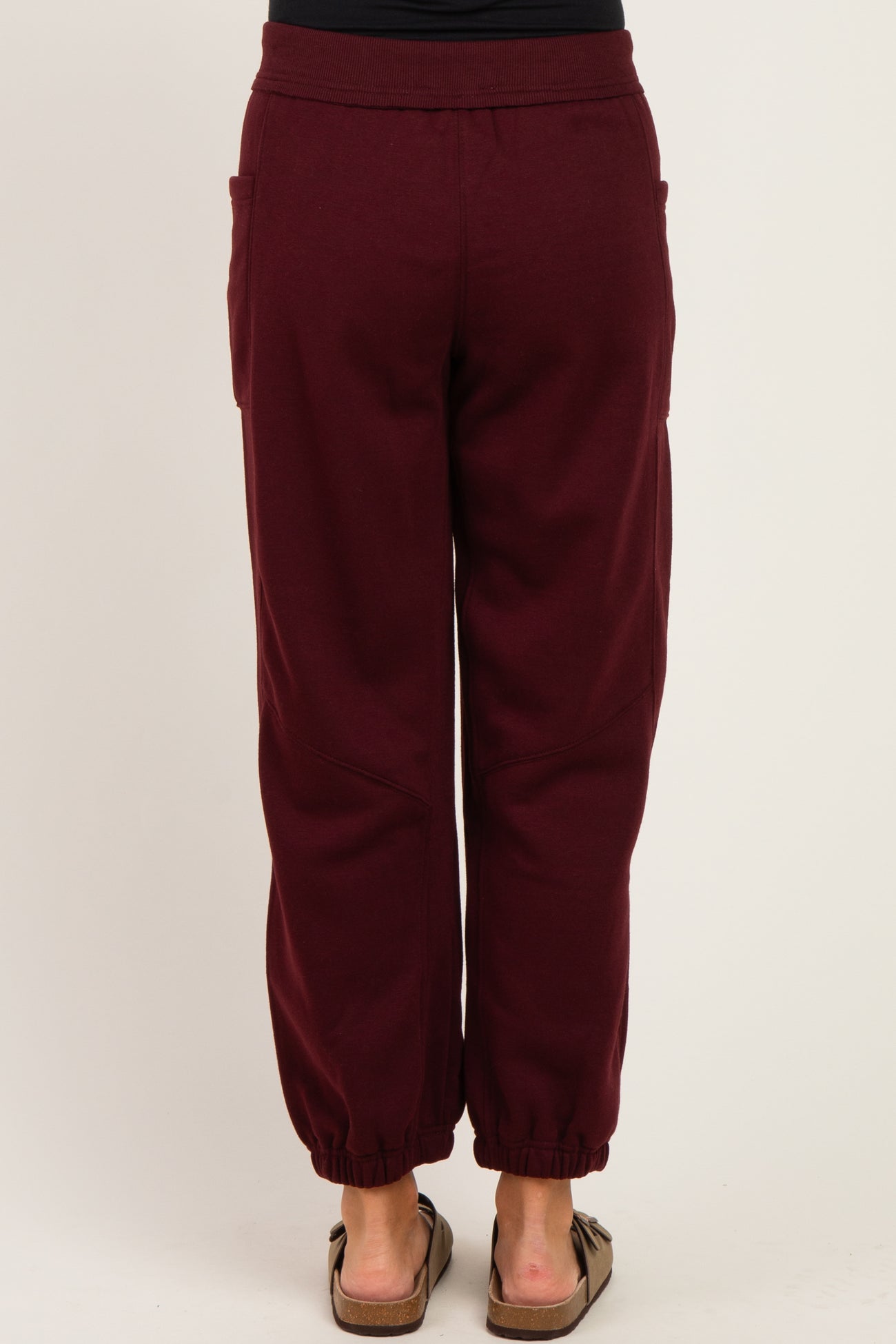 woman wearing burgundy maternity joggers with elastic ankle cuffs and side pockets, view from the back