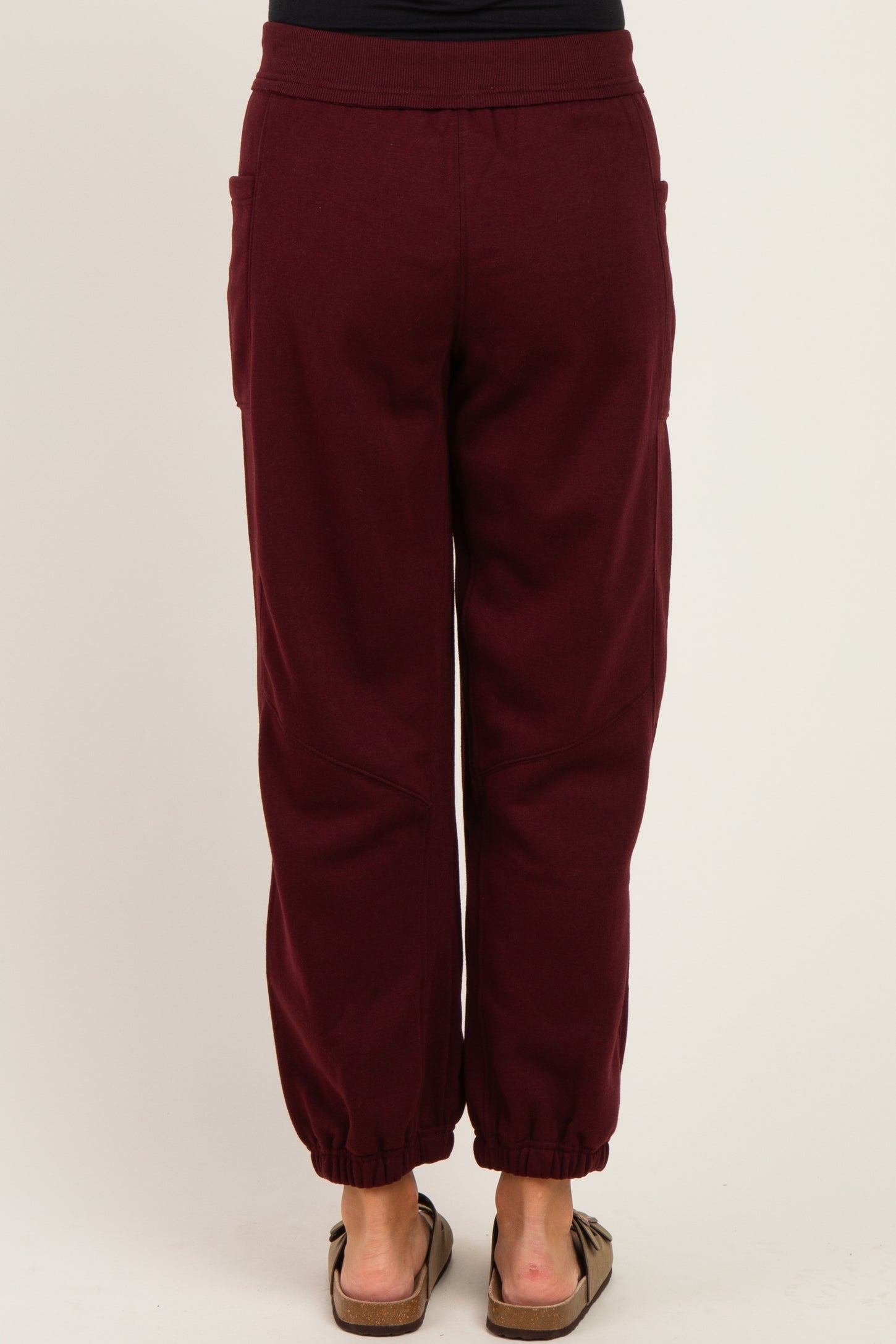 woman wearing burgundy maternity joggers with elastic ankle cuffs and side pockets, view from the back