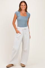 woman wearing a light blue short sleeve square neck bodysuit and white wide-leg sweatpants, standing with one hand in pocket