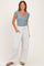 woman wearing a light blue short sleeve square neck bodysuit and white wide-leg sweatpants, standing with one hand in pocket