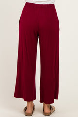woman wearing a pair of burgundy wide-leg pants with an elastic waistband, showing the back view and casual footwear