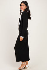 woman wearing a black long sleeve maxi dress with a contrasting white collar and a cropped cardigan, smiling at the side