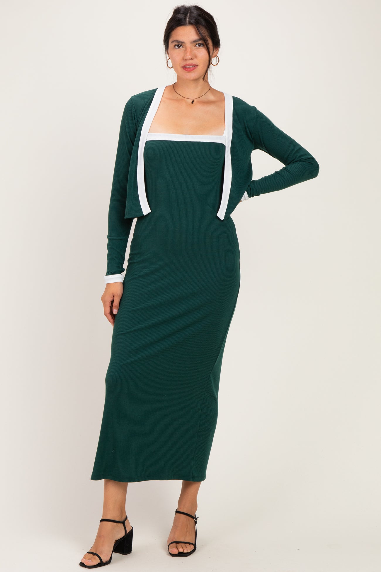 woman wearing a dark green ribbed maxi dress with a white trimmed open cardigan and strappy black heels