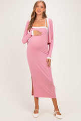 woman wearing a pink ribbed maternity dress with a side slit and a coordinating cardigan, holding her baby bump