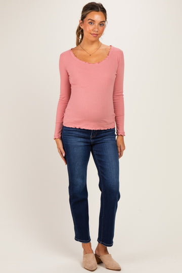 woman wearing a pink long sleeve maternity top with a scalloped neckline and a visible baby bump paired with dark blue jeans