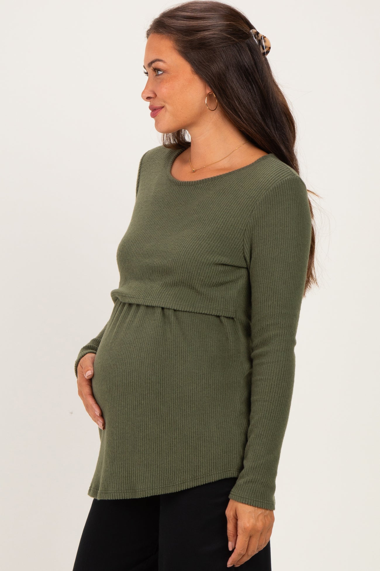 woman wearing a dark green maternity ribbed long sleeve top, gently holding her baby bump