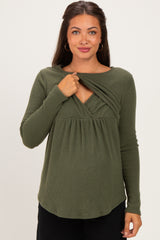 woman wearing a dark green maternity top with a layered front design and long sleeves, highlighting her baby bump