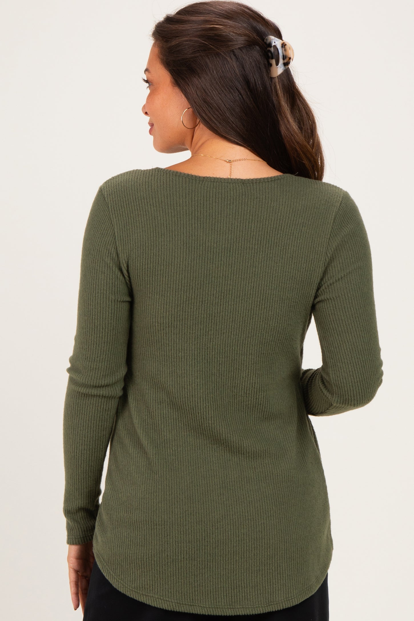 woman wearing a dark green ribbed maternity top, seen from the back, with long sleeves and a rounded hemline