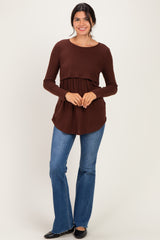 woman wearing a brown long sleeve top with a peplum waist and flared jeans, standing and smiling at the camera