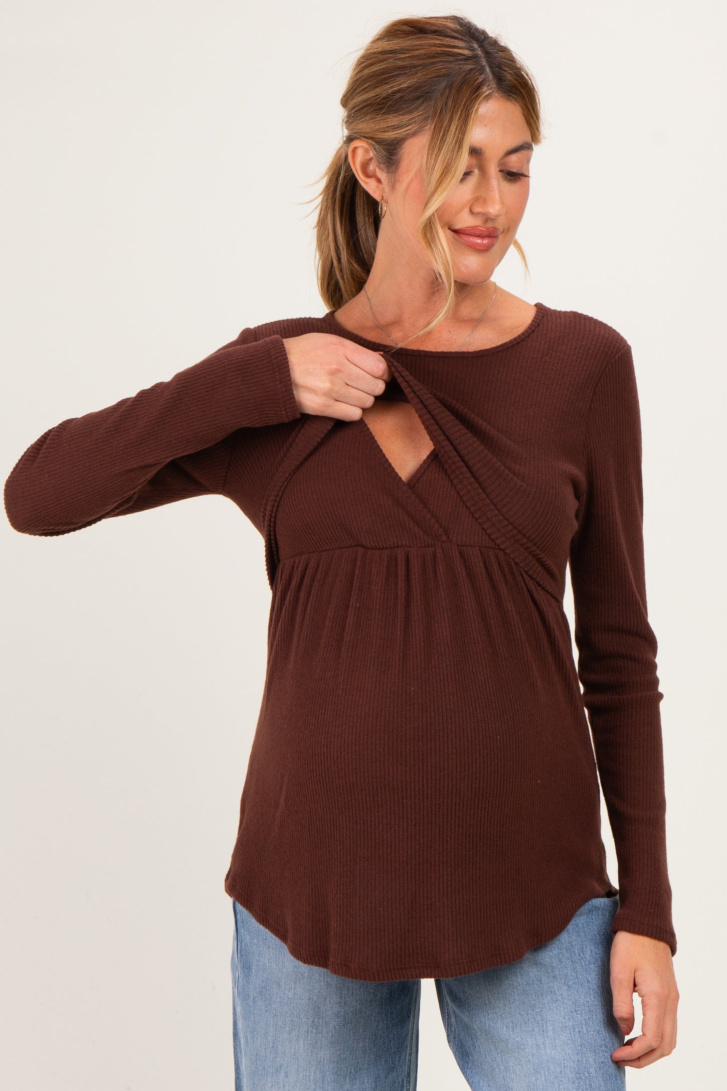 woman wearing a brown ribbed maternity top with a v-neck and lifting design to accommodate breastfeeding, showing her baby bump