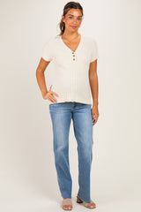 woman wearing a cream ribbed maternity top with short sleeves and button details, showing her baby bump and paired with light blue jeans