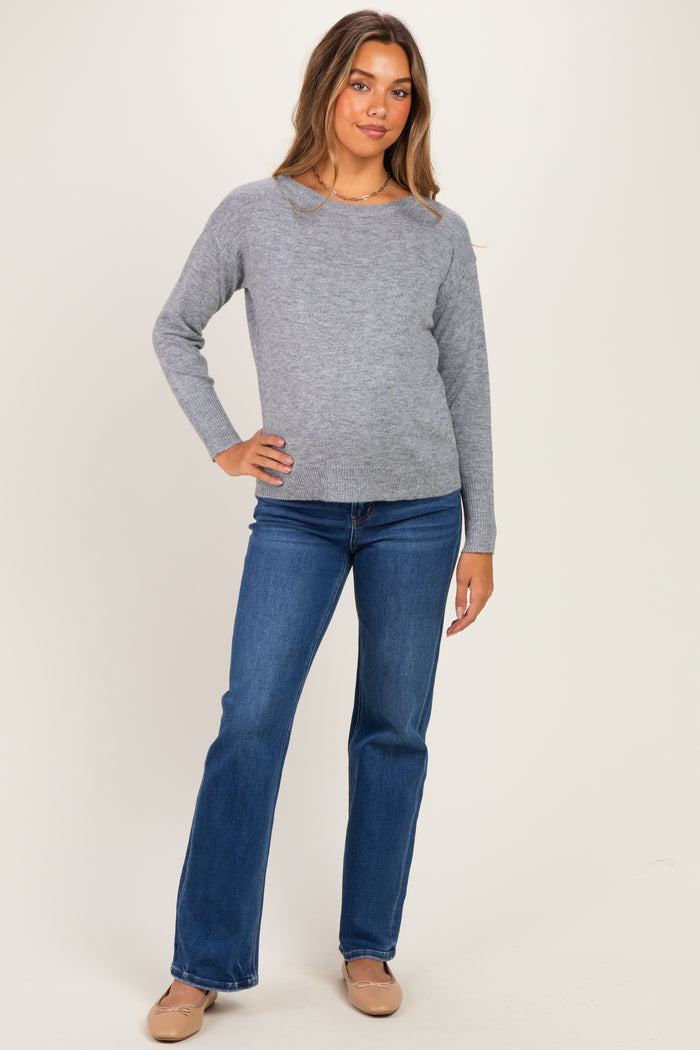 woman wearing a light gray long sleeve maternity sweater and blue flared jeans, with a subtle baby bump visible