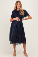 woman wearing a navy blue floral maternity dress with sheer sleeves and a baby bump visible