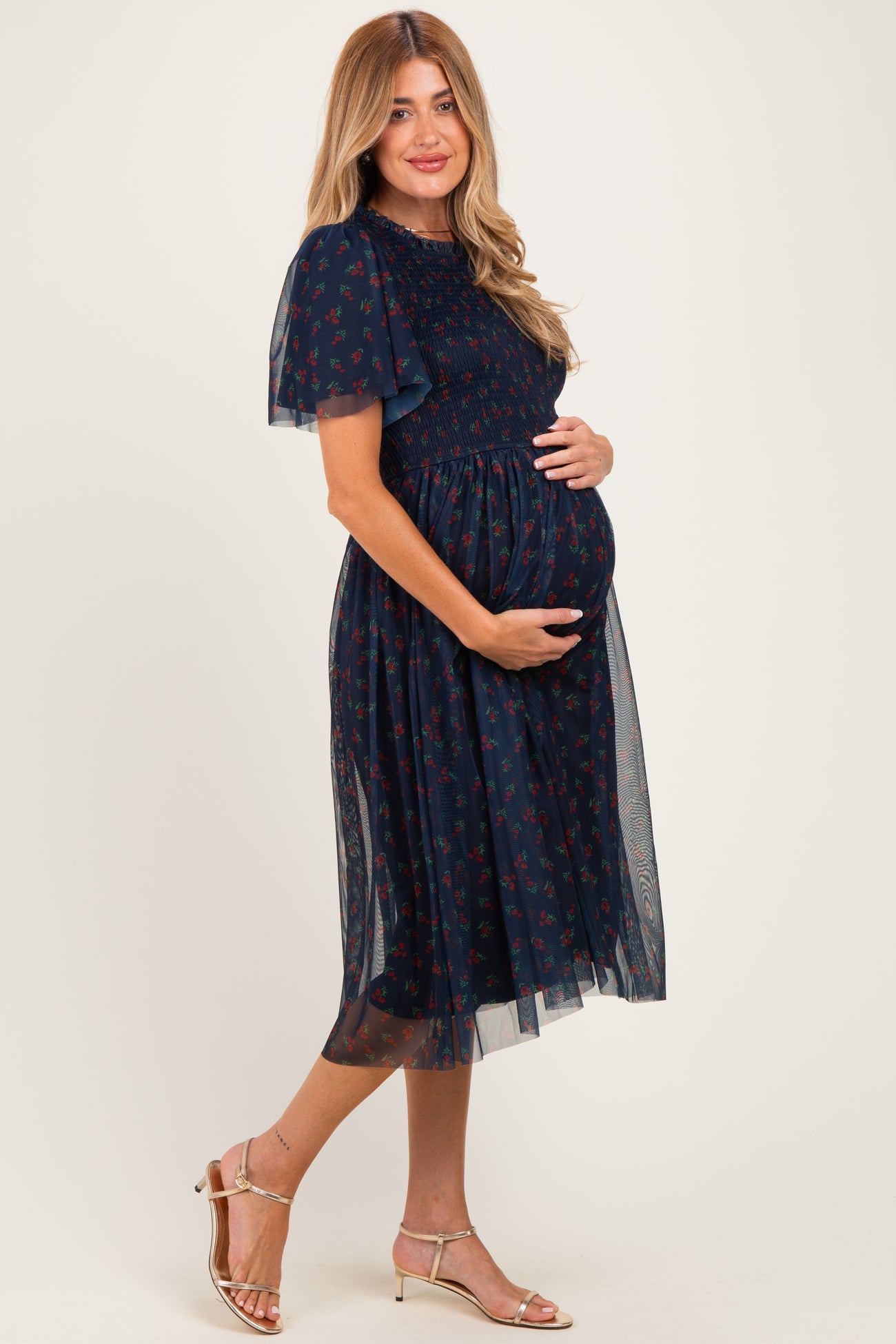 woman wearing a navy blue floral maternity dress with sheer sleeves and holding her baby bump