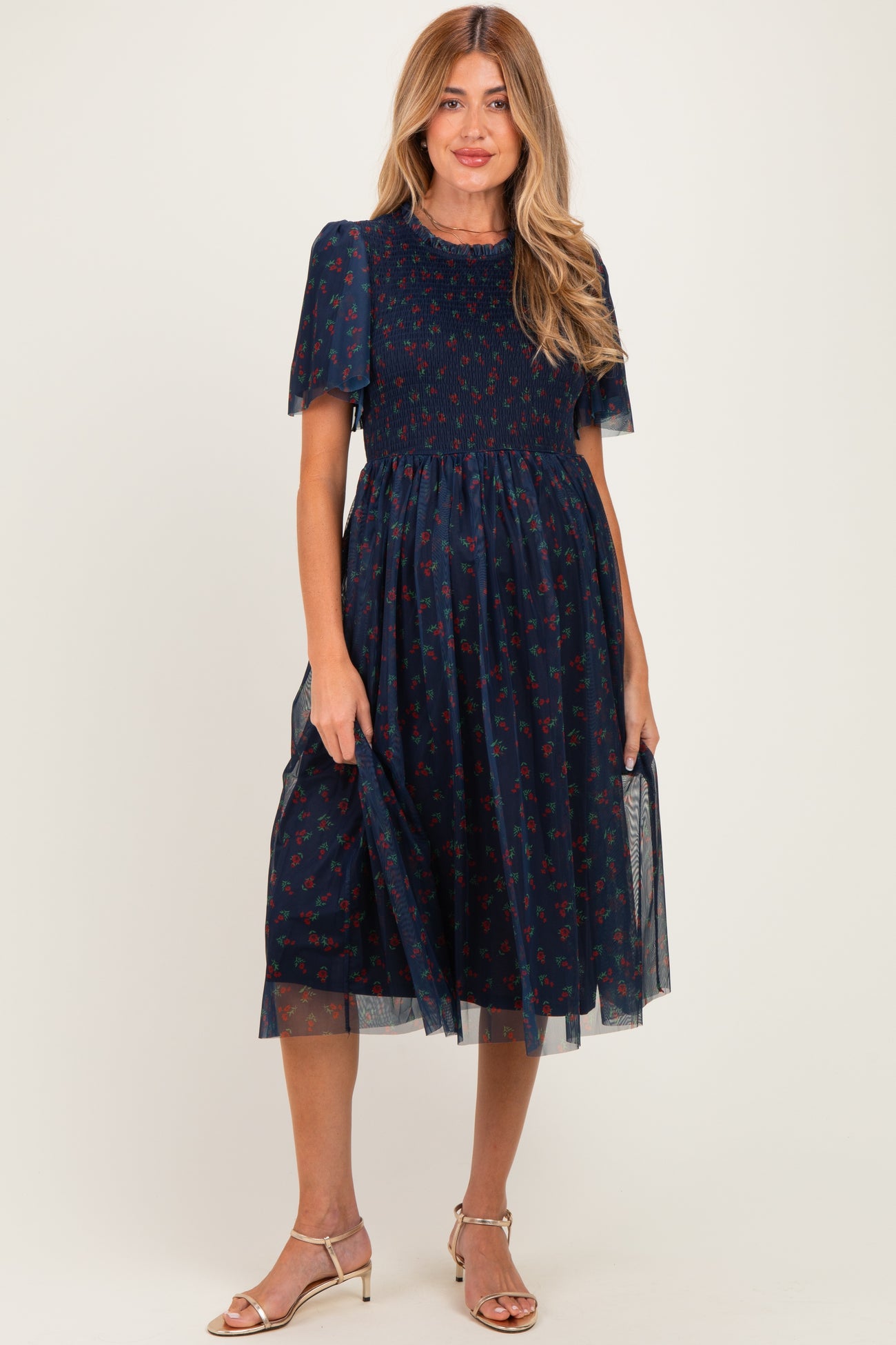 woman wearing a navy maternity dress with floral print and sheer puff sleeves, holding the skirt to show off the baby bump