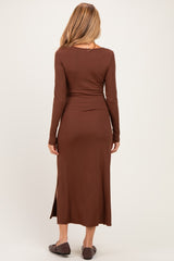 woman wearing a brown long sleeve maternity dress with a fitted silhouette and side slit, showing her baby bump from the back